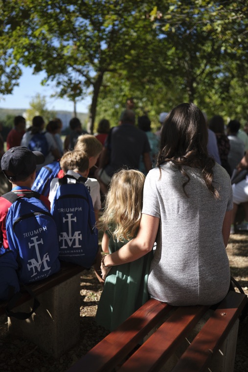 Pilgrims with Triumph backpacks seated on benches under the trees