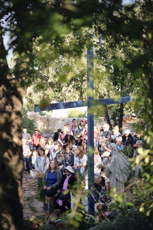 Pilgrims praying beneath the trees at a blue cross