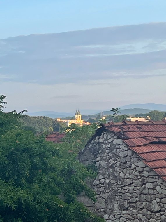 A church tower on the hills in the evening, beyond an old stone roof