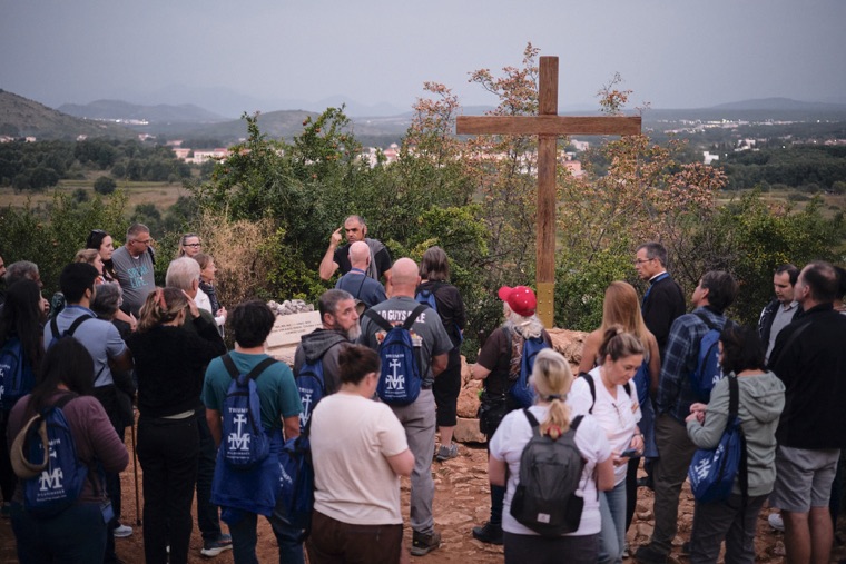 Pilgrims praying together at a wooden cross on the hilltop
