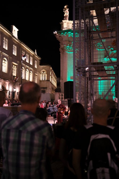 An evening crowd in the old town, a church lit in green