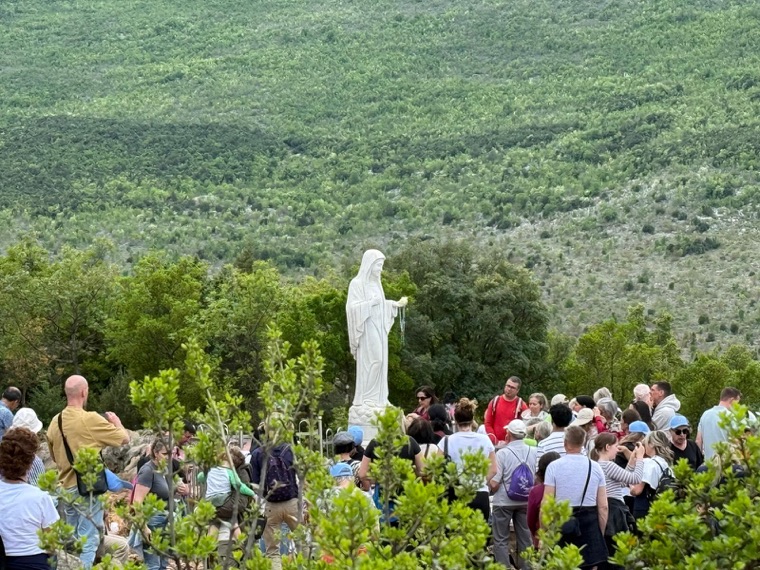 Pilgrims gathered on the green hillside below the statue